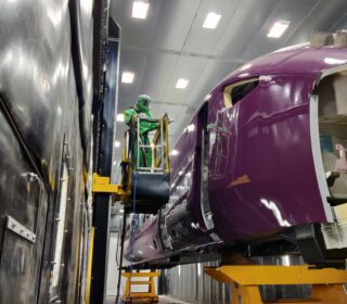 Blast operator in full GVS RPE blasting PPE holding a blast hose and nozzle processing rolling stock inside the blast room at Hitachi Rail.