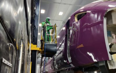 Blast operator in full GVS RPE blasting PPE holding a blast hose and nozzle processing rolling stock inside the blast room at Hitachi Rail.