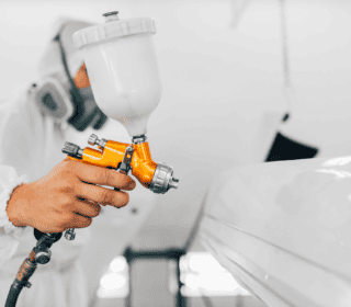 stock image of a spray gun being operated on a piece of vehicle in a spray booth