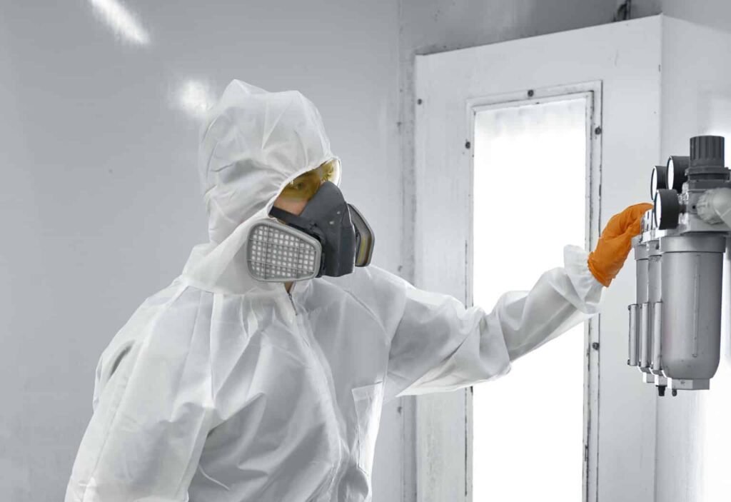 Paint sprayer inside a automotive spray booth in full PPE