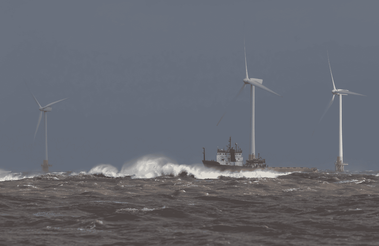 Ship sailing in rough sea around offshore wind farm turbines.