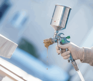 Close-up of a clogged spray gun dripping paint from the nozzle during use.