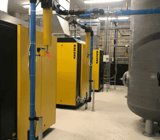A clean, well-organised compressor room featuring yellow KAESER air compressors and blue air piping.