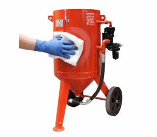 A person wearing blue gloves cleaning a red blast pot with a white cloth.