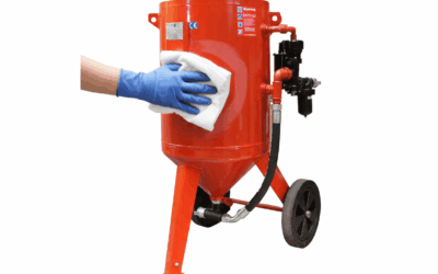 A person wearing blue gloves cleaning a red blast pot with a white cloth.